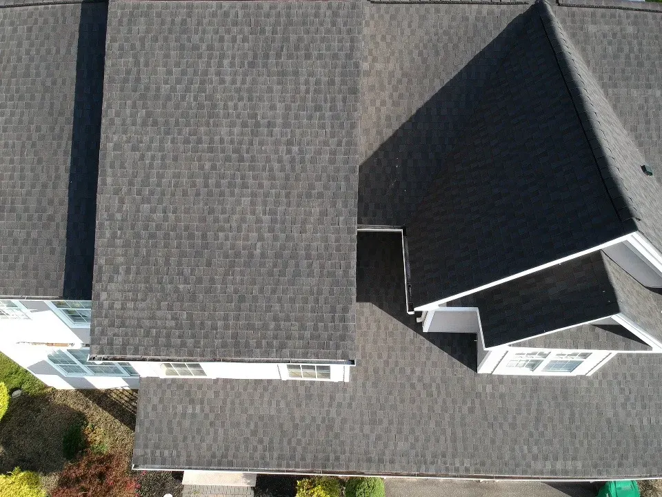 A finished charcoal shingle roof seen straight down from above, with clean ridge and valley lines and white gutters along the edges.